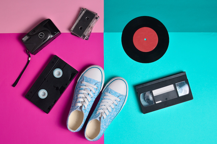 Keds, vinyl records, audio cassettes, video cassettes, plastic vintage camera, are laid out on a neon colored surface. Entertainment 90s. Top view. Flat lay.